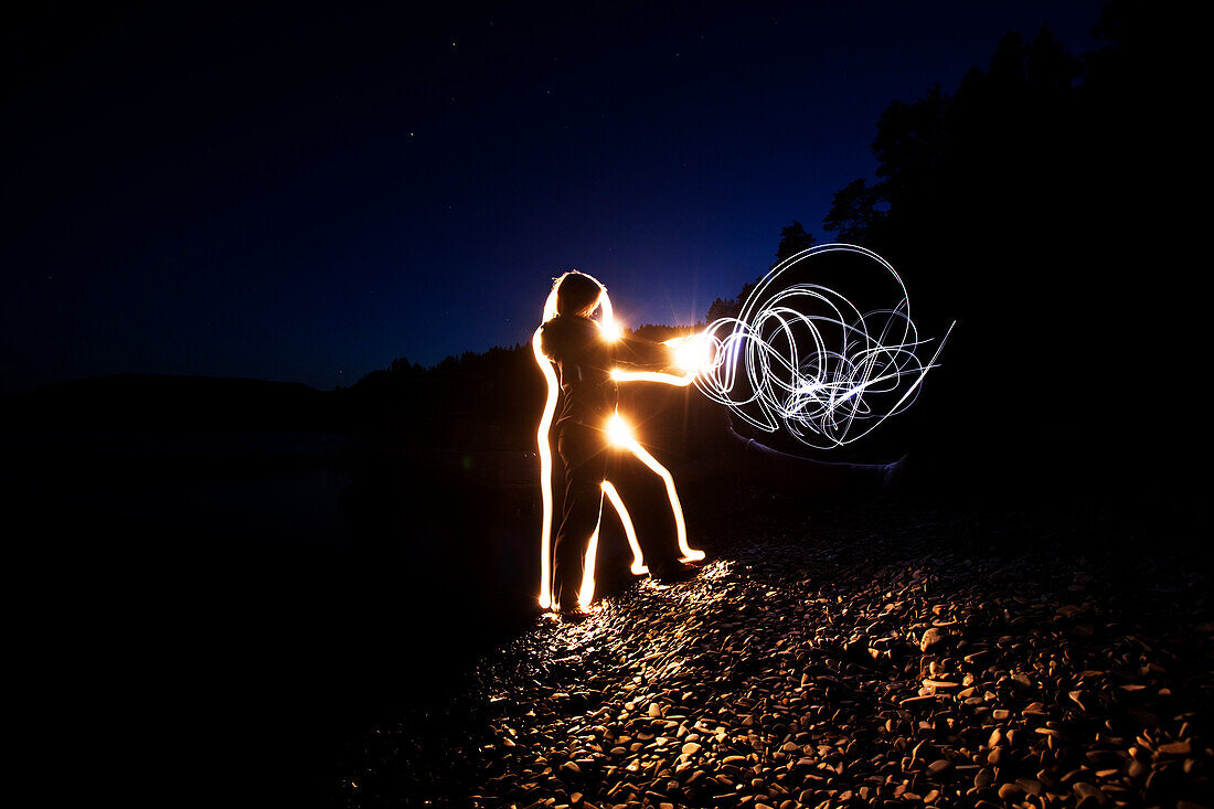 A woman sends energy through her body and out her hands at sunset in Idaho. This light painting image was created with a long exposure and flash lights Sandpoint, Idaho, USA