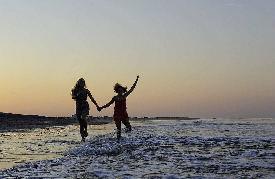 Two young women play in the surf at sunset/, Massachusetts, USA