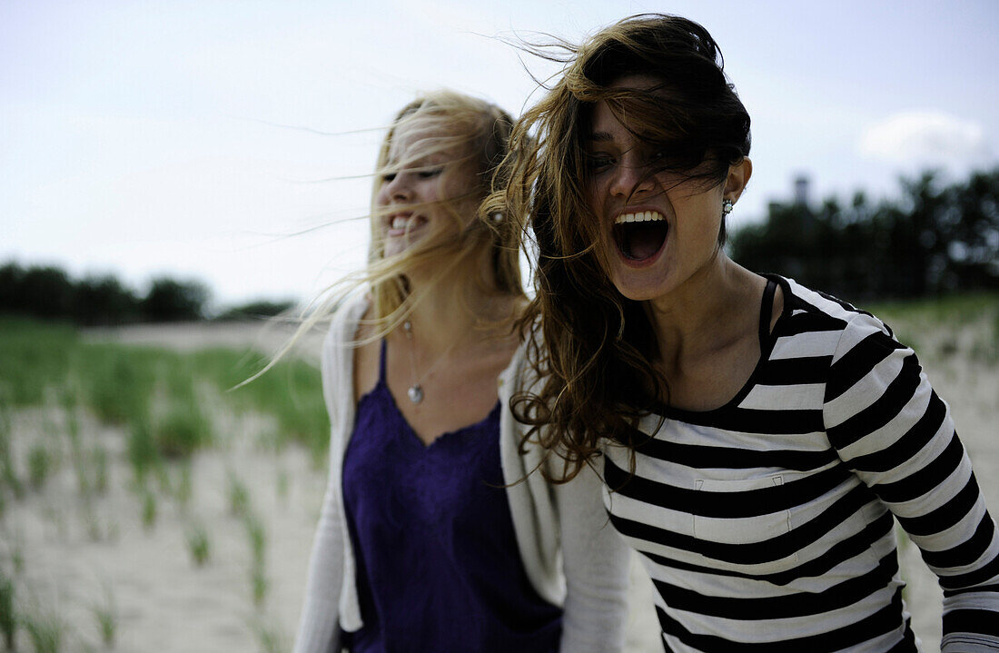 Two women laugh in the wind at the beach Cape Cod, Massachusetts, USA