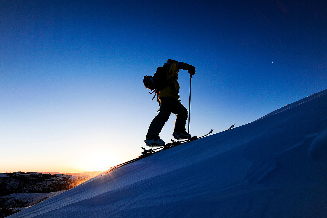A silhouette of a skier skinning up a snow covered slope at sunrise in the Sierra Nevada near Lake Tahoe, California Carson Pass, California, USA