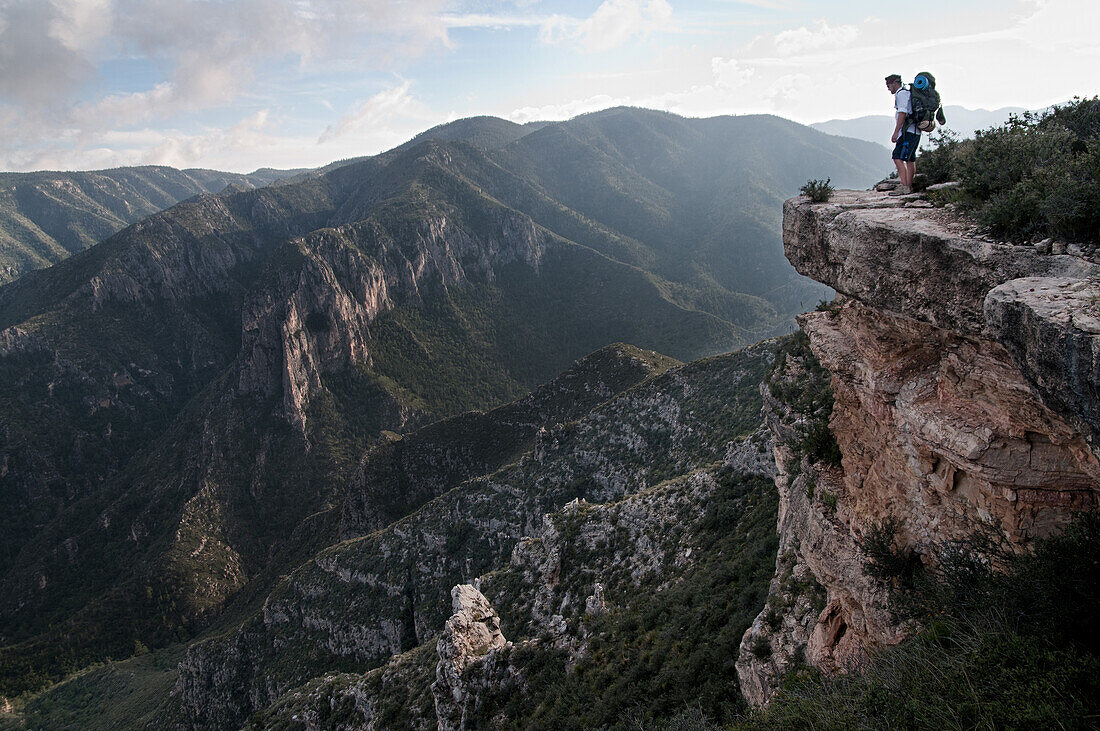 A backpacker peers over a ledge into McKittrick Canyon at Guadalupe National Park Texas, USA