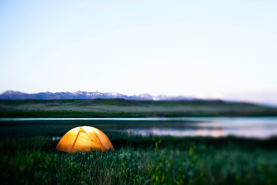 A glowing tent next to a lake at sunset in Montana Bozeman, Montana, USA