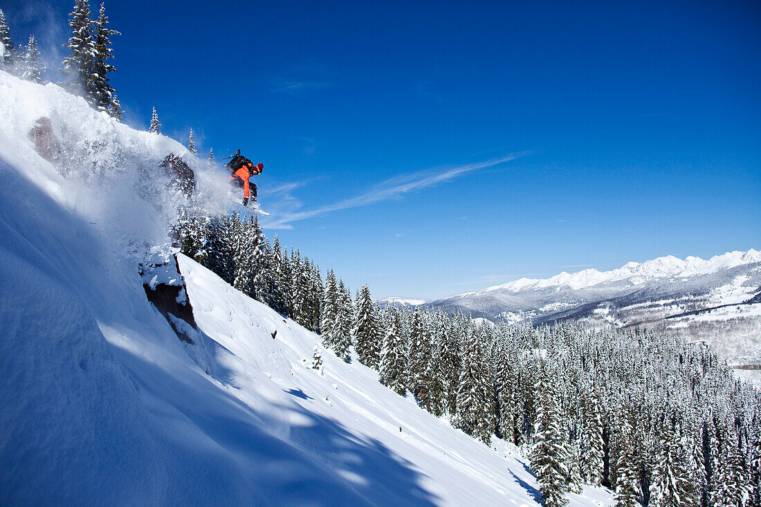 A athletic snowboarder jumping off a cliff on a sunny powder day in Colorado Vail, Colorado, USA