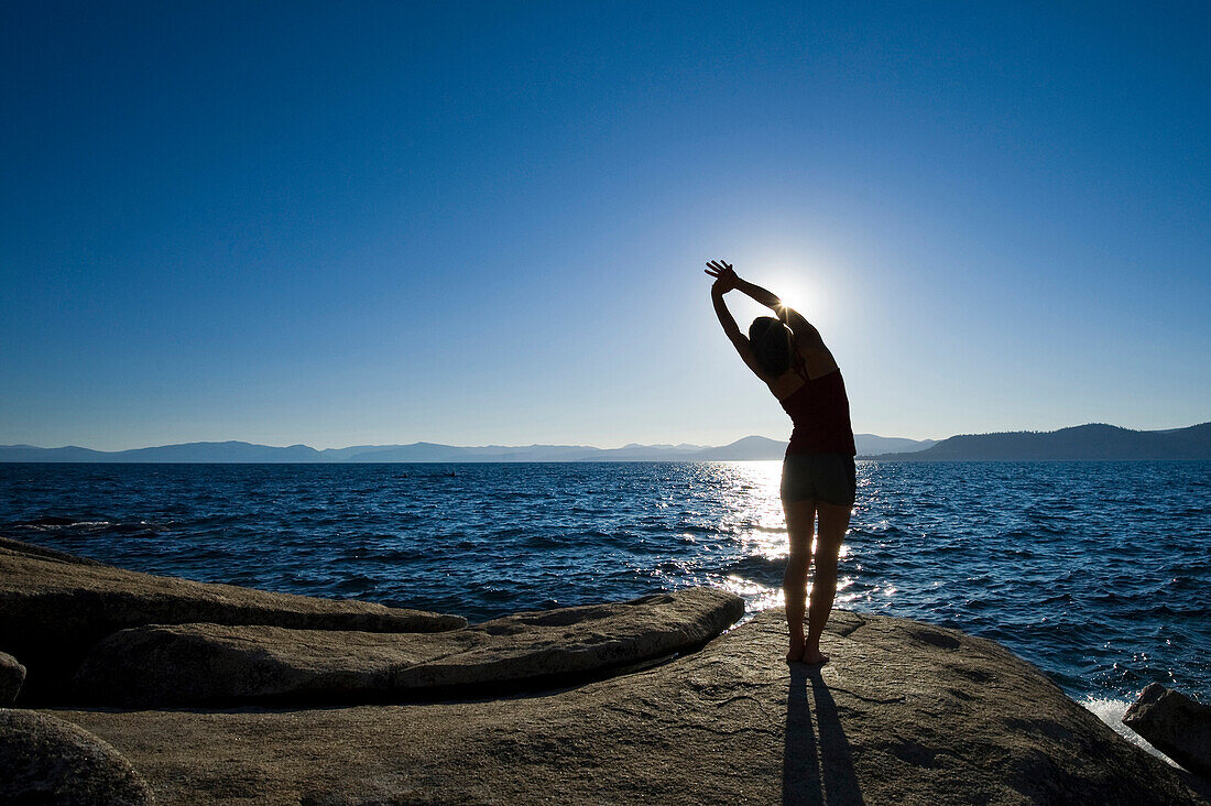 A silhouette of a woman stretching on a granite boulder on the east shore of Lake Tahoe in the summer, NV Lake Tahoe, Nevada, USA