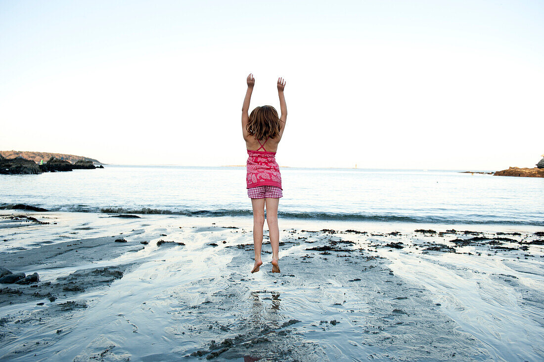 a girl jumps in the air at the beach in southern maine, portland, me, usa