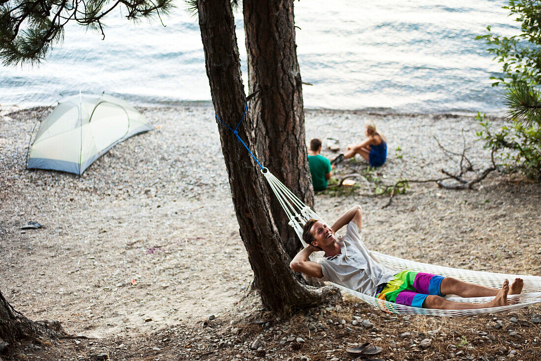 A group of young adults camping laugh and smile next to a lake Idaho., Sandpoint, Idaho, USA