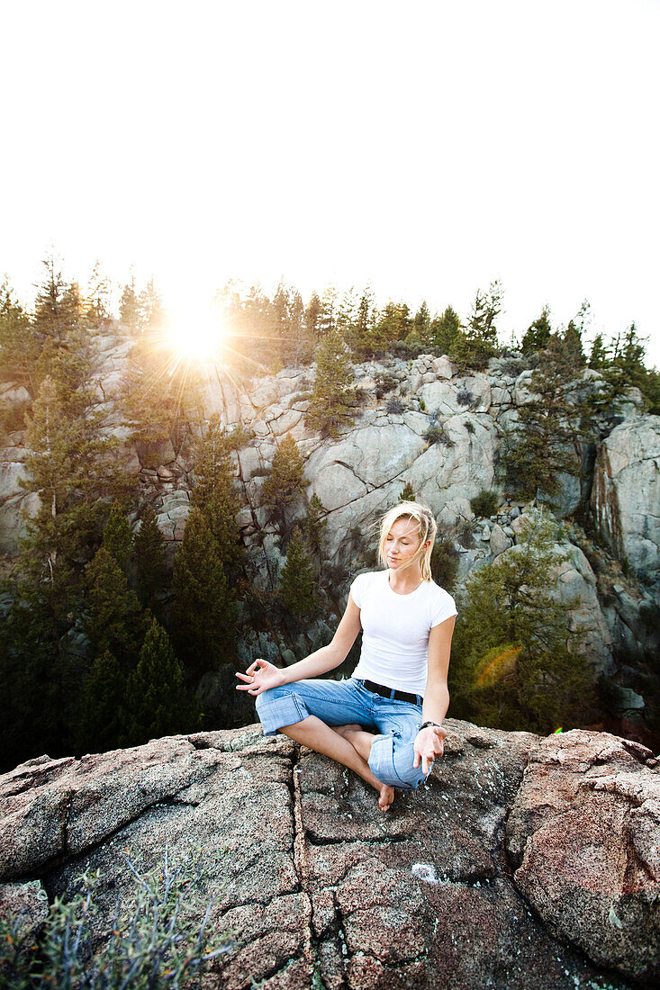 A beautiful young woman meditating on a cliff at sunset in Montana., Butte, Montana, USA