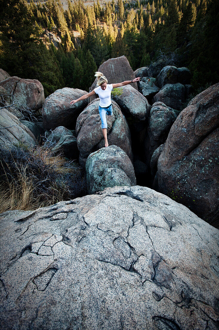 A athletic young woman leaping across a boulder field in Montana., Butte, Montana, USA