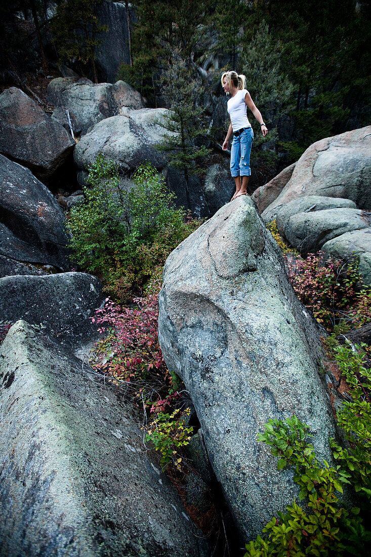A athletic young woman looks over the edge of a large boulder in Montana., Butte, Montana, USA
