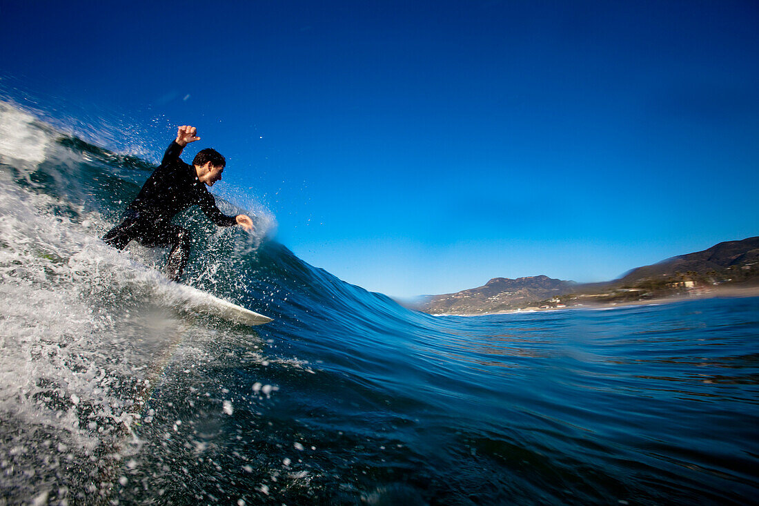 A male surfer sets up for a backside barrel while surfing at Zuma Beach in Malibu, California., Malibu, California, United States of America