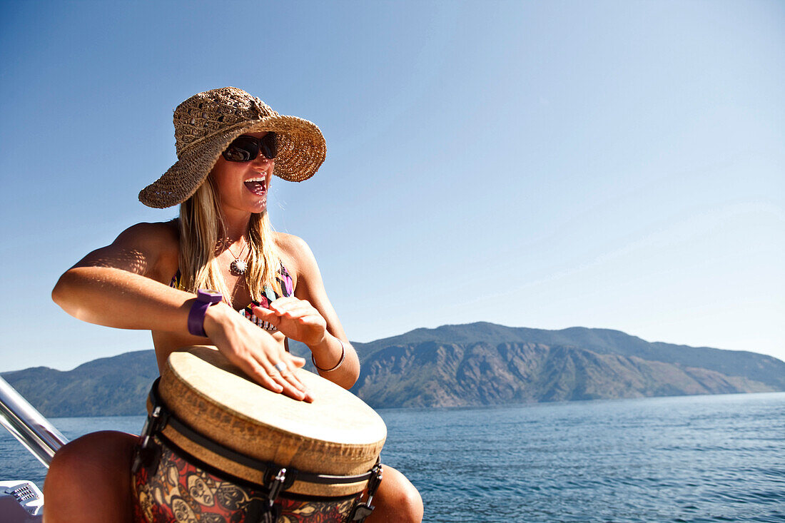 A happy young woman smiling plays a drum on the edge of a beautiful lake in Idaho., Sandpoint, Idaho, USA