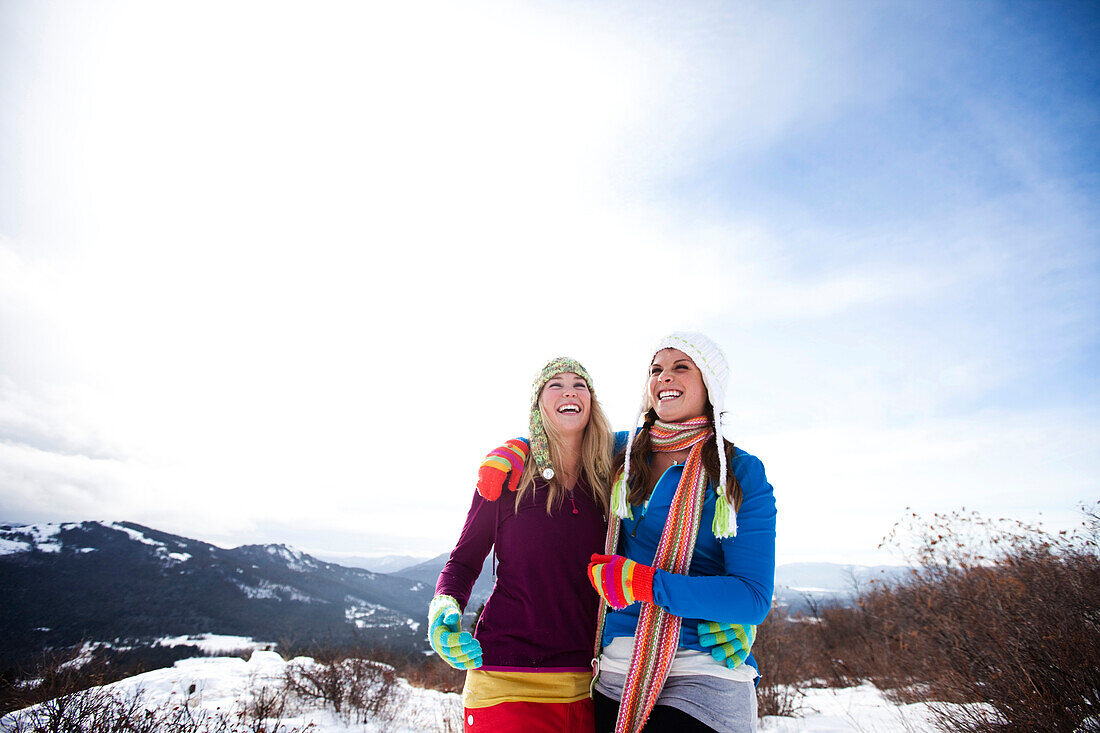 Two young women laugh and smile while hiking in the snow on a beautiful winter day in Idaho., Sandpoint, Idaho, USA