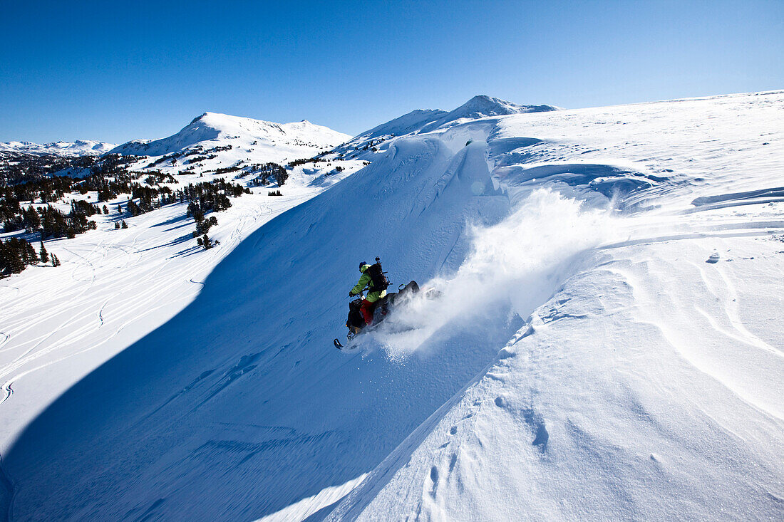 A snowmobiler jumping off a cornice on a sunny winter day in Montana., Bozeman, Montana, USA