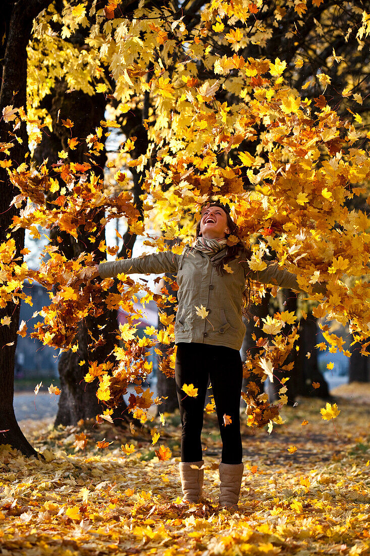 A beautiful young woman smiling throws orange leaves into the air surrounded by fall colors in Idaho., Sandpoint, Idaho, USA