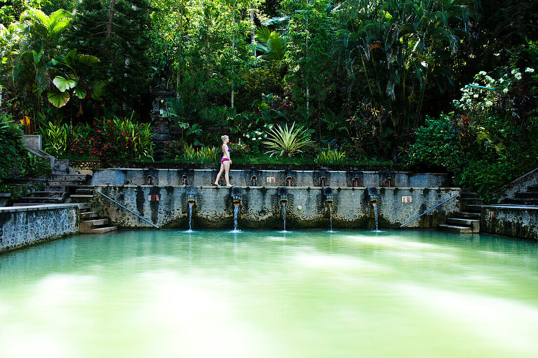 A beautiful woman relaxing next to a hot springs surrounded by a lush jungle and flowers in Bali, Indonesia., Lovina, Bali, Indonesia