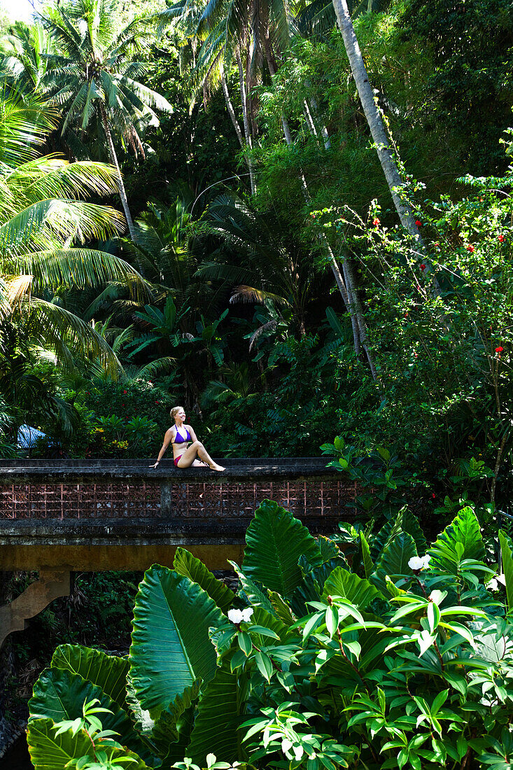A beautiful woman relaxing on a bridge next to a hot springs surrounded by a lush jungle and flowers in Bali, Indonesia., Lovina, Bali, Indonesia
