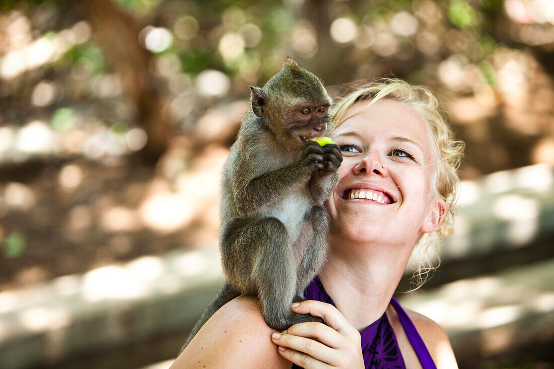 A woman smiling as a monkey eats on her shoulder in Bali, Indonesia., Uluwatu, Bali, Indonesia