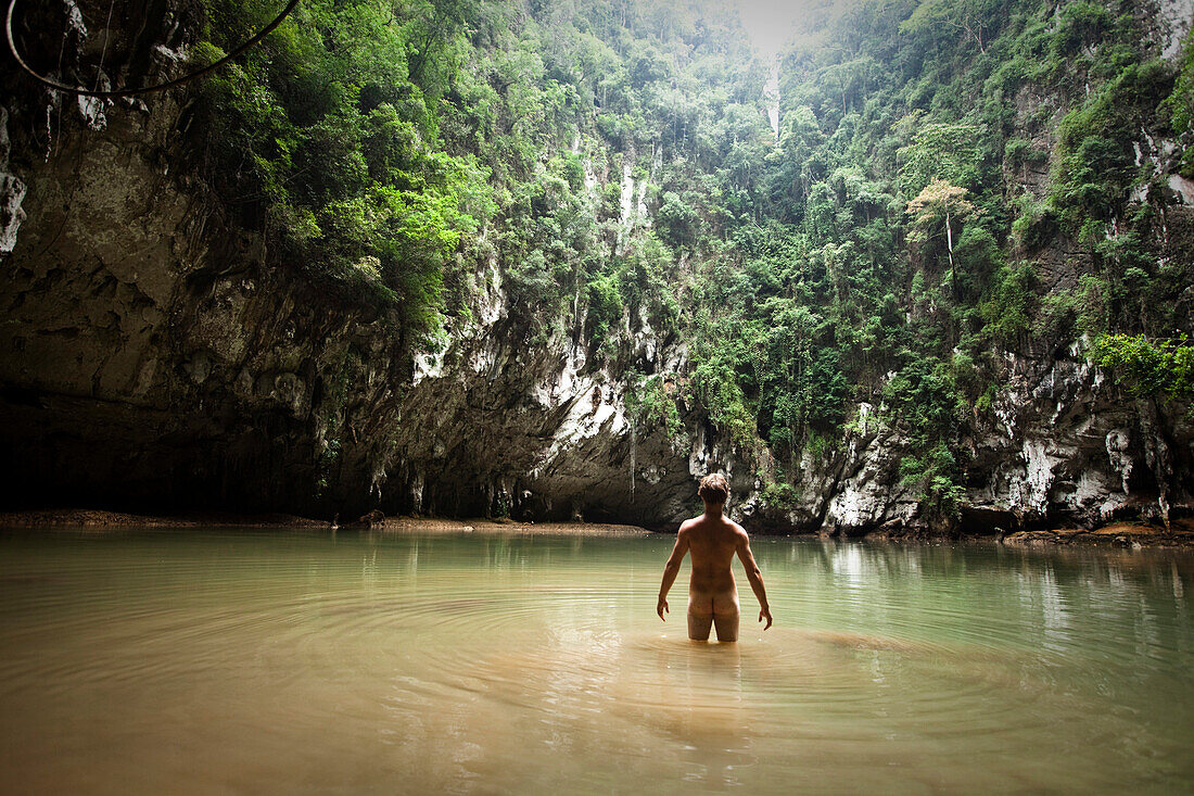 A athletic young man adventuring deep into a remote jungle pool stands naked in Thailand., Railay, Thailand