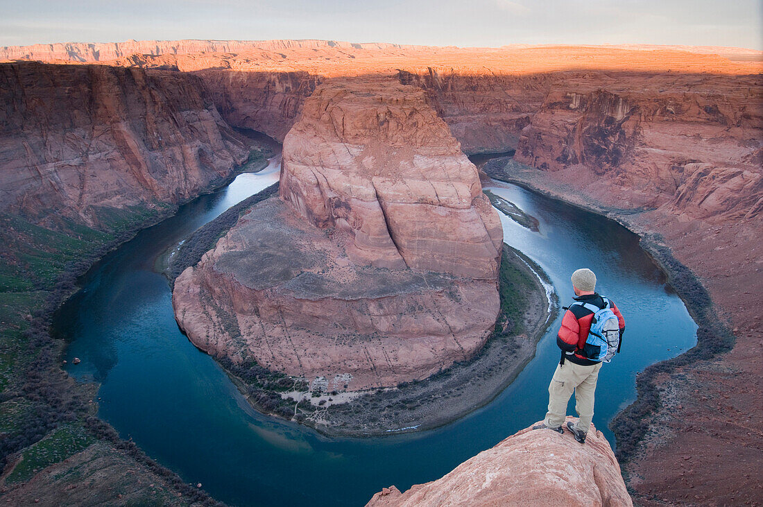 Male hiker watching the sunrise at the Horseshoe Bend Overlook with the Colorado River below, Page, Arizona., Page, Arizona, usa