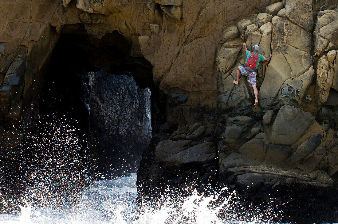 A man rock climbing near a blow hole, Big Sur, California., Big Sur, California, usa