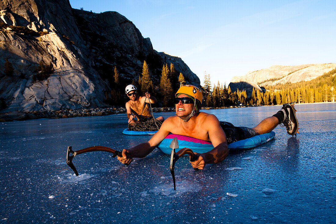 An ice climber works his way across Tenaya Lake in Yosemite, California while getting a belay from a fellow climber in a pool raft., Yosemite, California, United States of America