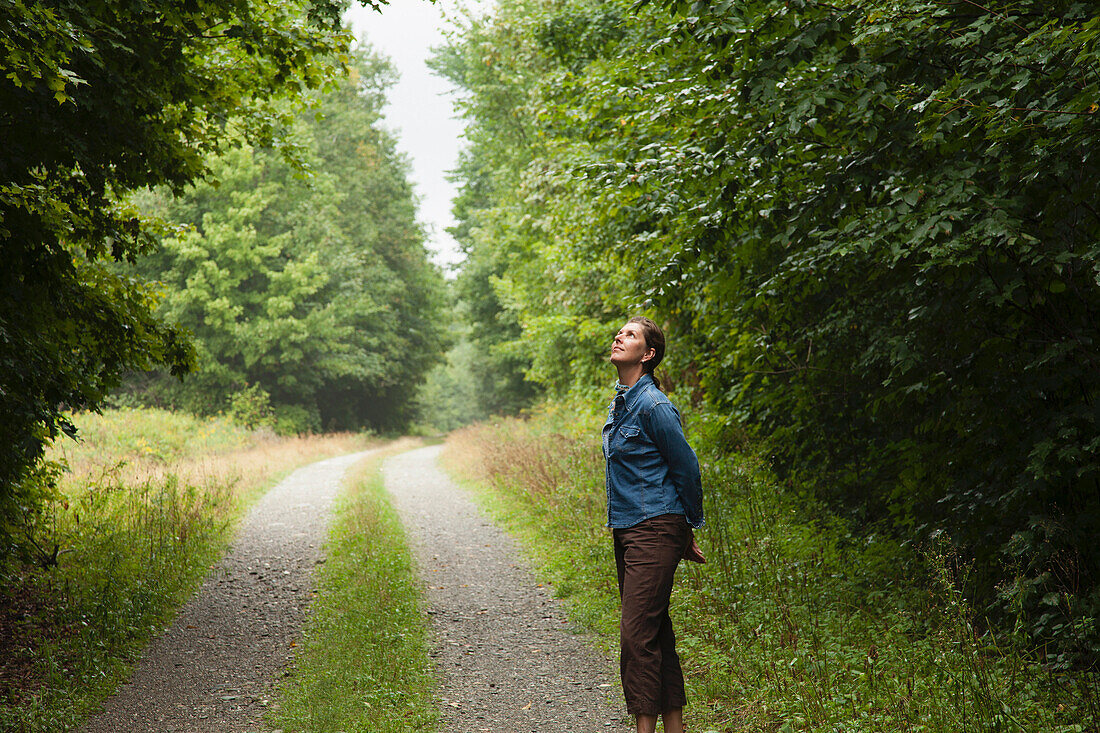 A woman standing in a clearing on an empty road in the  woods of northern Maine, near Spencer Pond., Maine, USA