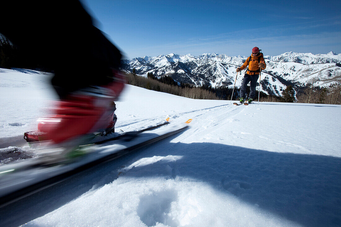 Low angle perspective of a skier's boot motion blurred with a skier int he background., Park City, Utah, USA
