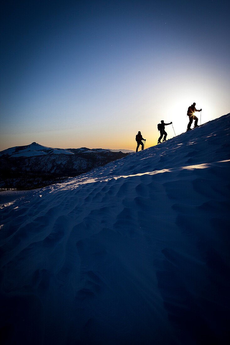 Three backcountry skiers silhouetted in beautiful sunrise light., South Lake Tahoe, California, USA