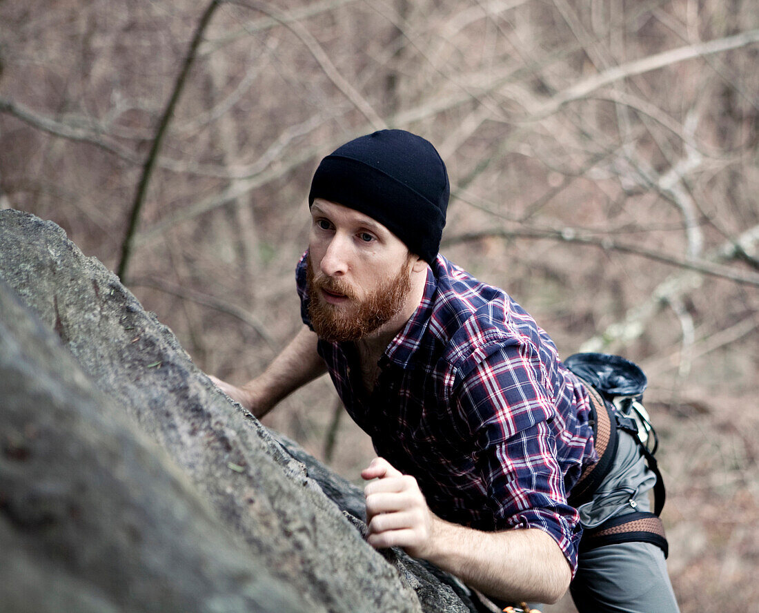 A male rock climber with a beard scales the side of a cliff., Erving, MA, USA