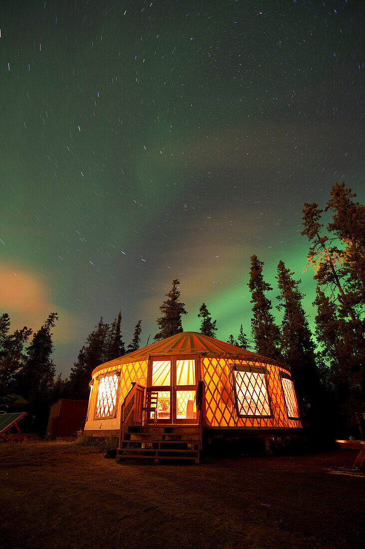 The Aurora Borealis (Northern Lights) over an illuminated yurt outside of Whitehorse in the Yukon Territory, Canada., Whitehorse, Yukon Territory, Canada