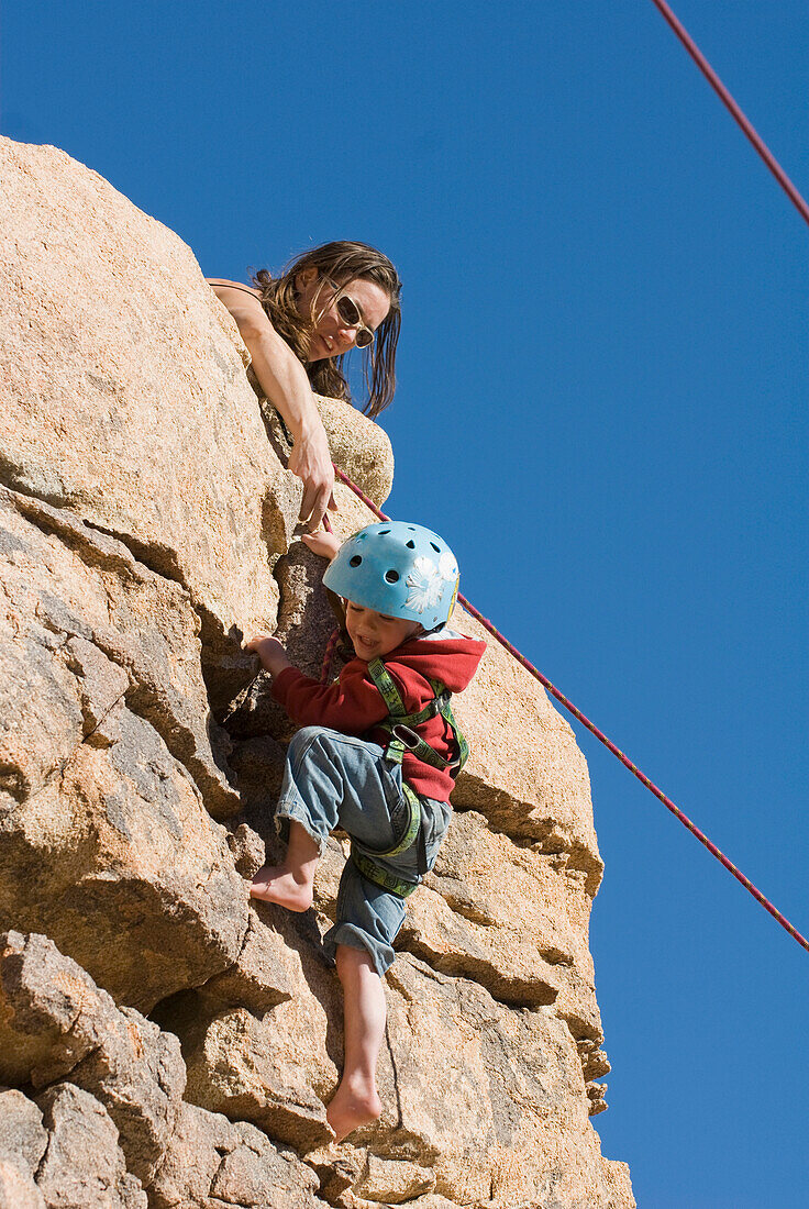 Mother helping child finish a rock climb, Joshua Tree National Park, California 29 Palms, California, USA