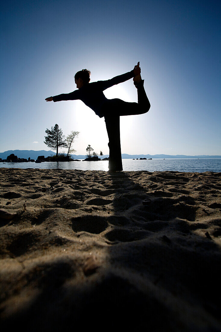 Silhouette of a woman doing yoga on a beach by a lake in the mountains South Lake Tahoe, California, USA