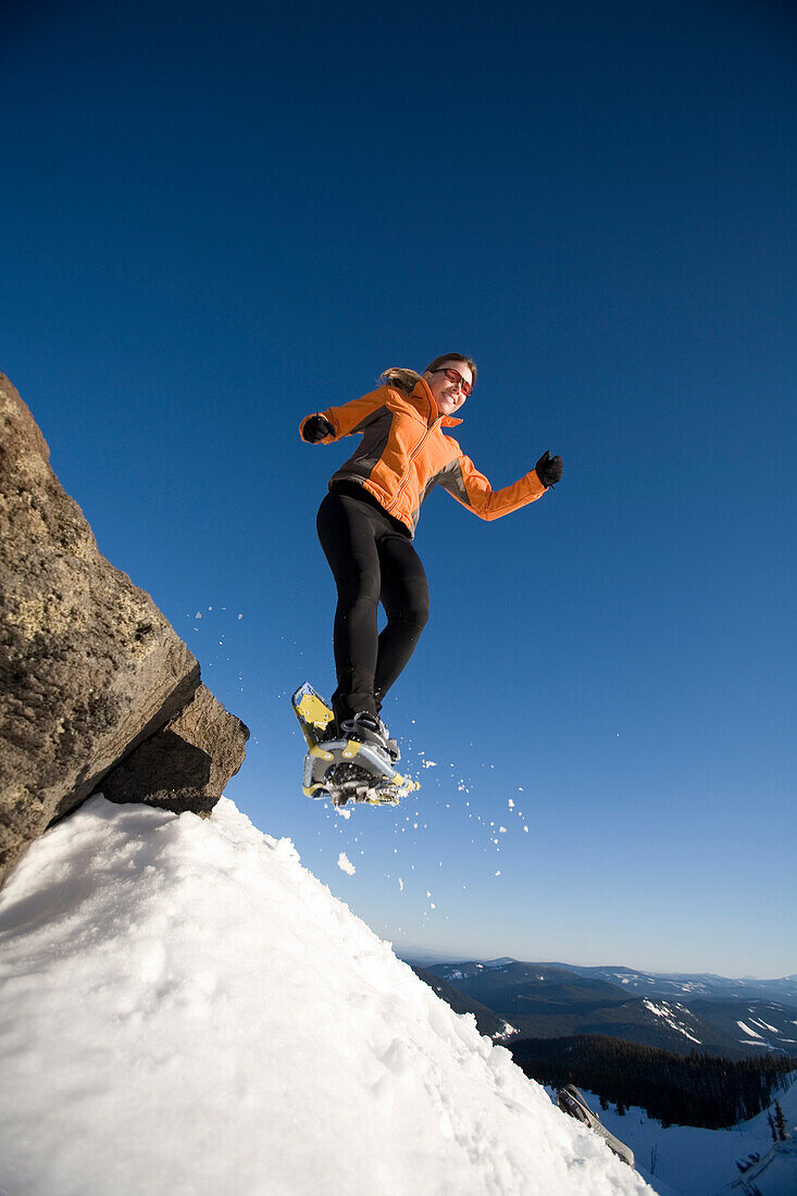 Woman jumps off rock with snowshoes Mount Hood, Oregon, USA