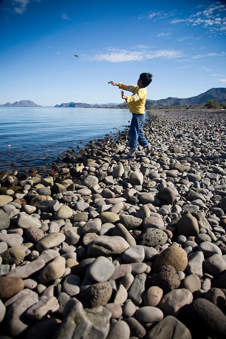 A young boy throws a stone into a large body of water in Loreto, Baja California Sur, Mexico Loreto, Baja, Mexico