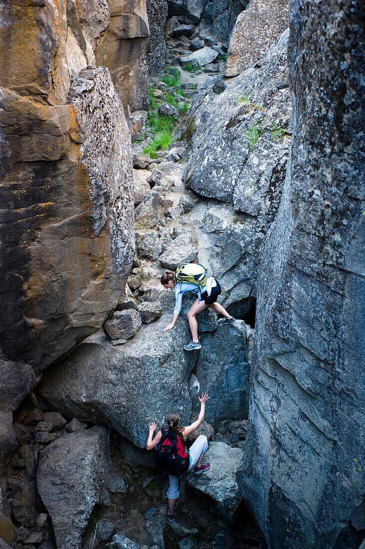 Two women climb through Crack In the Ground, a volcanic fissure near Christmas Valley, Oregon Christmas Valley, Oregon, USA