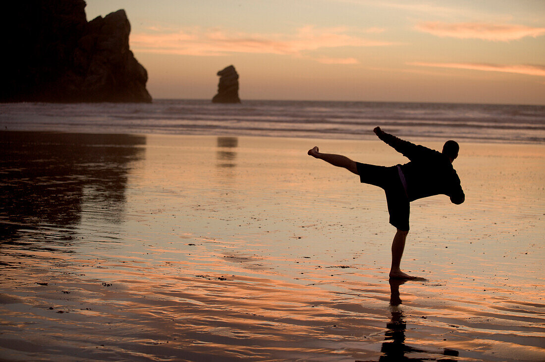 One mid adult man practices Taekwondo on the beach at sunset in Morro Bay, California Morro Bay, California, USA