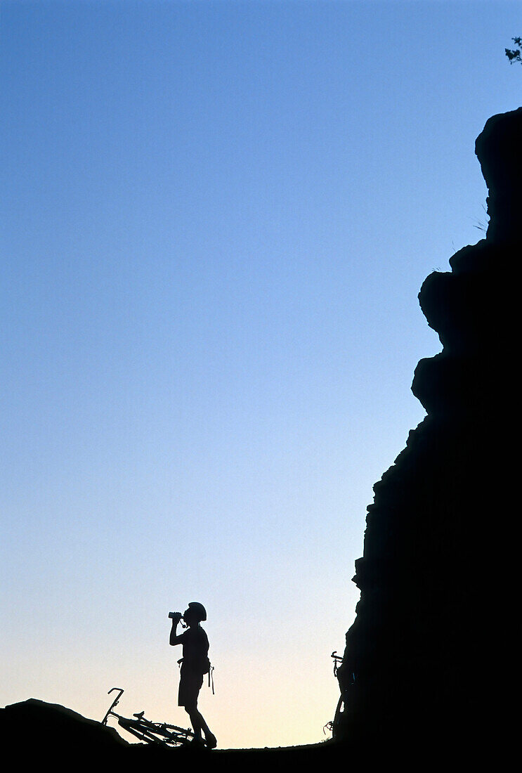 Silhouetted male mountain biker taking a water break Bozeman, Montana, USA