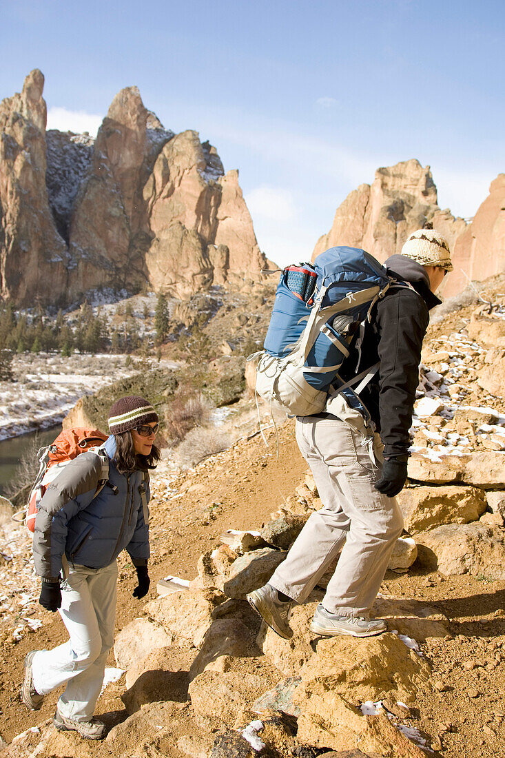 Two rock climbers with backpacks walking down a trail with a cliff in the background Terrebone, Oregon, USA