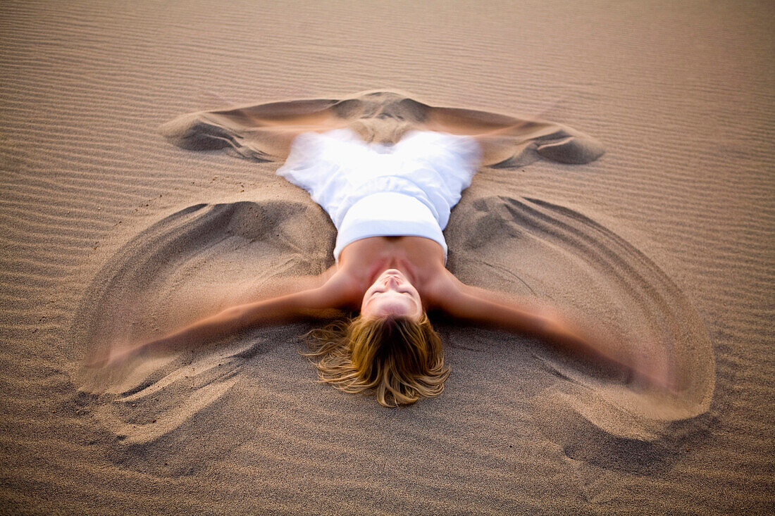 A woman in white making a sand angel on the Stovepipe Wells Dunes in Death Valley, California Death Valley, California, USA