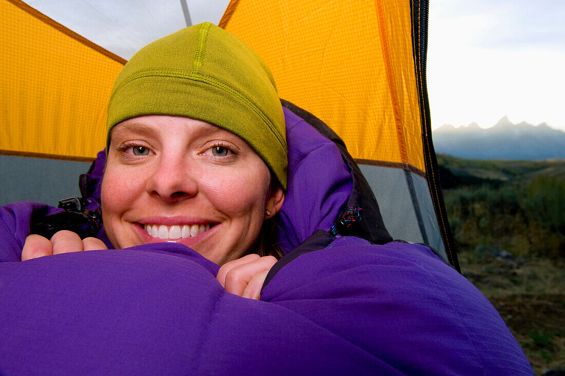 A young woman smiles in her sleeping bag and tent while camping in Grand Teton National Park, Wyoming Jackson, Wyoming, USA