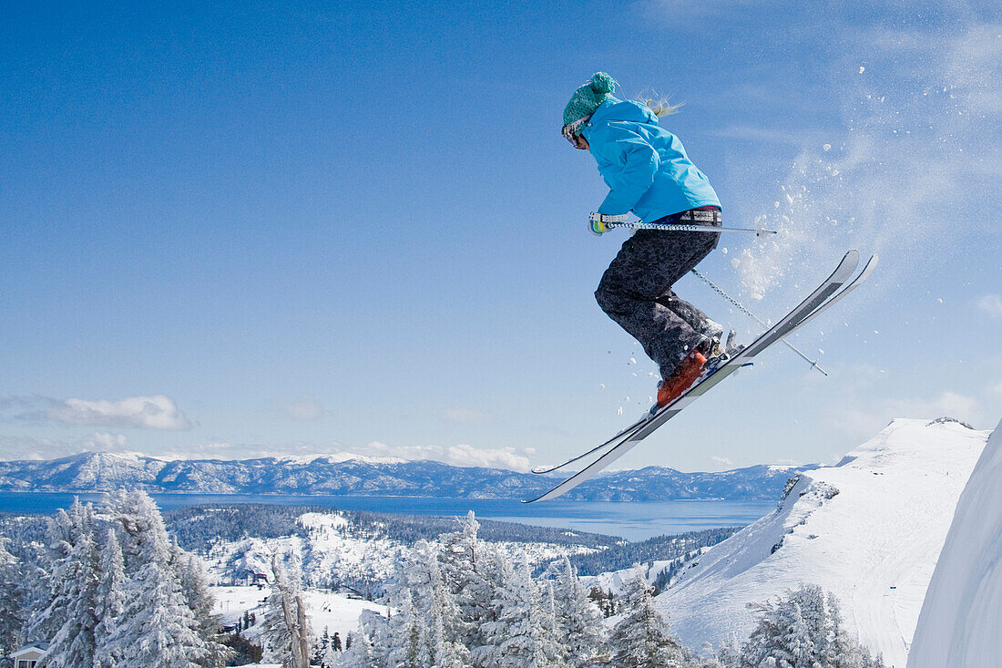A female skier launching into fresh powder snow with mountains and blue sky in the background Squaw Valley, California, USA