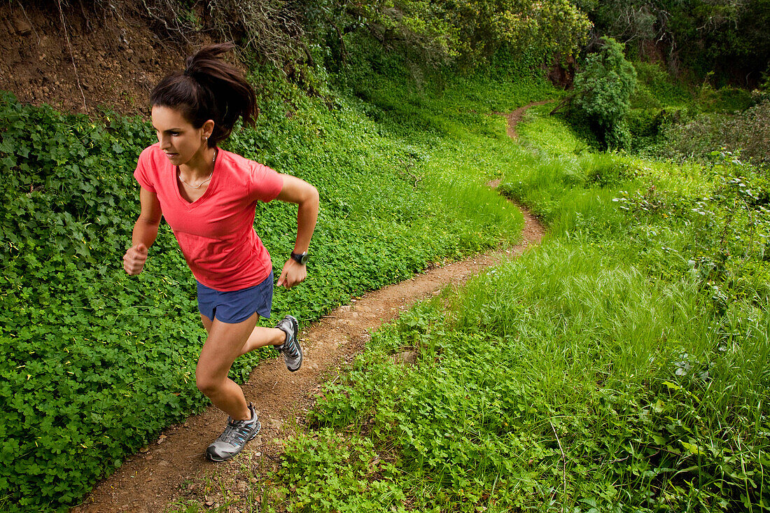 Woman trail running through a green meadow in the woods Montecito, California, USA
