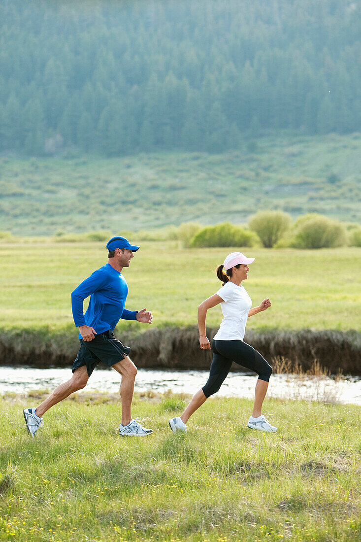 An athletic couple trail running through a field next to a river South Lake Tahoe, California, USA
