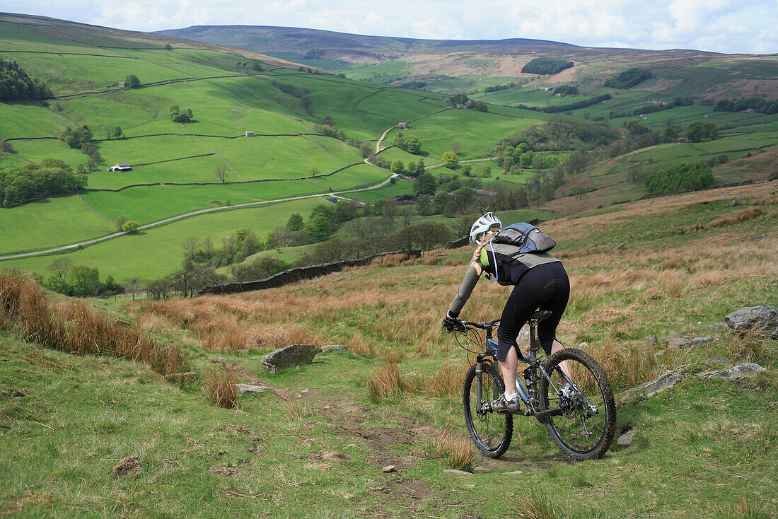 A woman mountain bides down a steep trail in the Yorkshire Dales area of England England