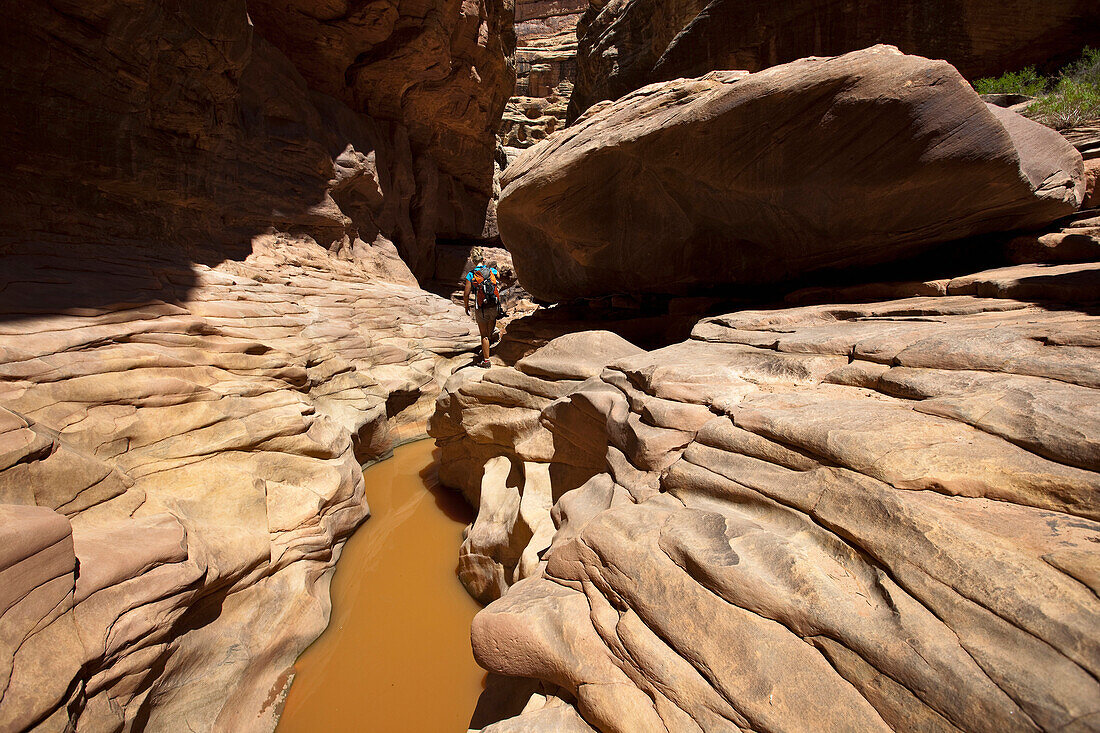 A woman hiking through a canyon with water and interesting rock formations in Utah Utah, USA