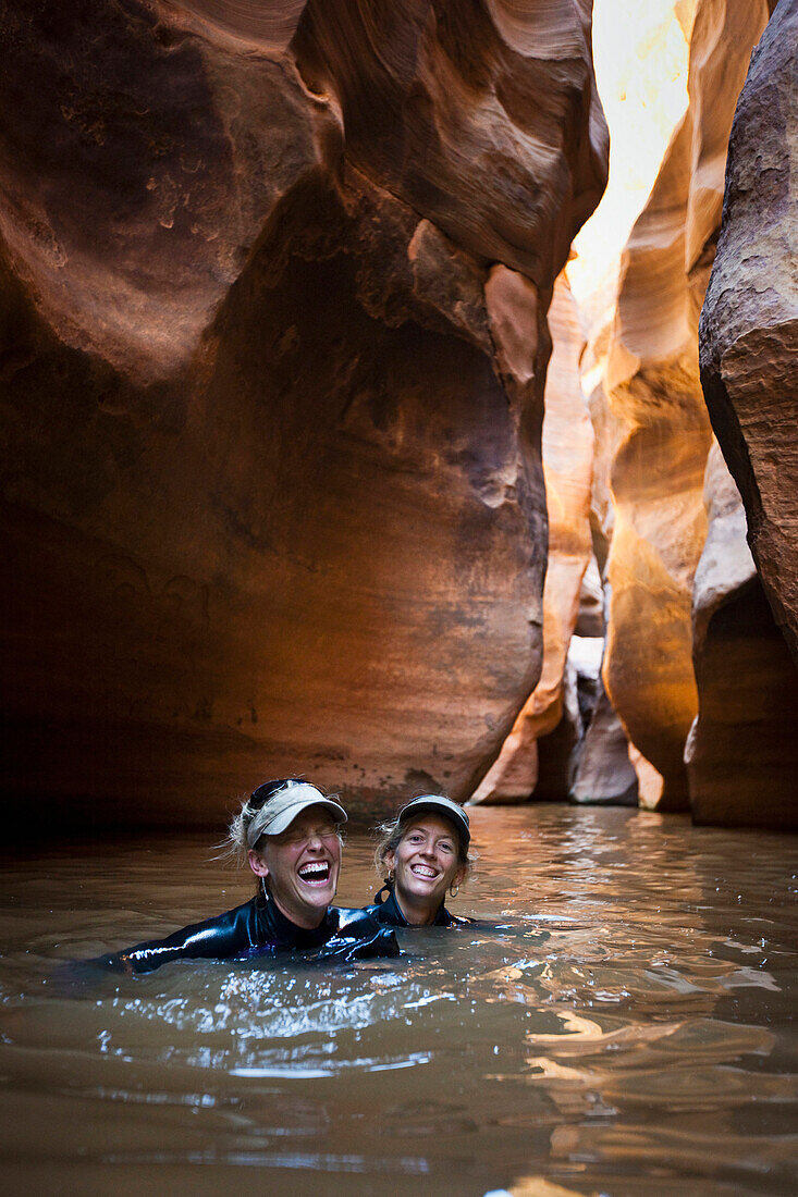 Two women laughing while wading through a deep pool in a slot canyon in Utah Utah, USA