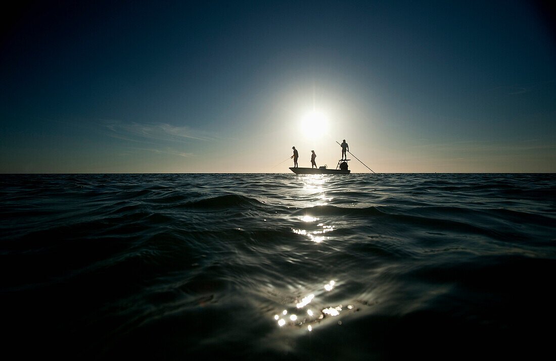 A couple fish as a man pilots a small boat in Florida. (silhouette), Key West, Florida, USA