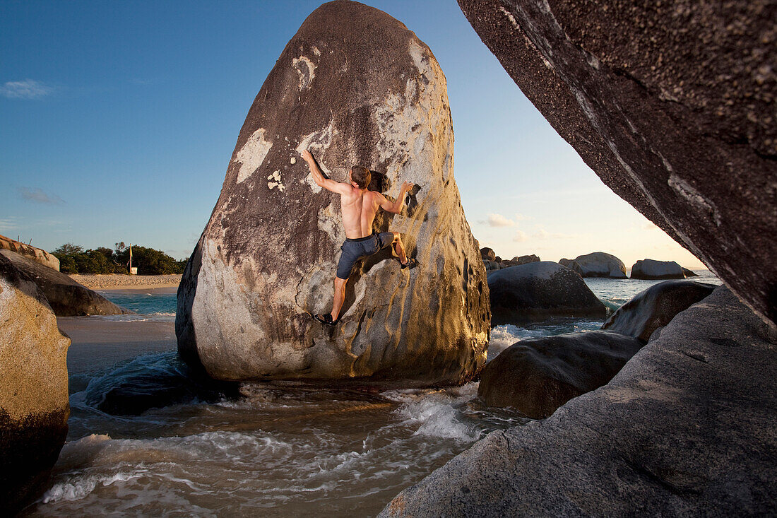A male climber climbs a boulder surrounded by high tide at sunset the British Virgin Islands Virgin Gorda, British Virgin Islands