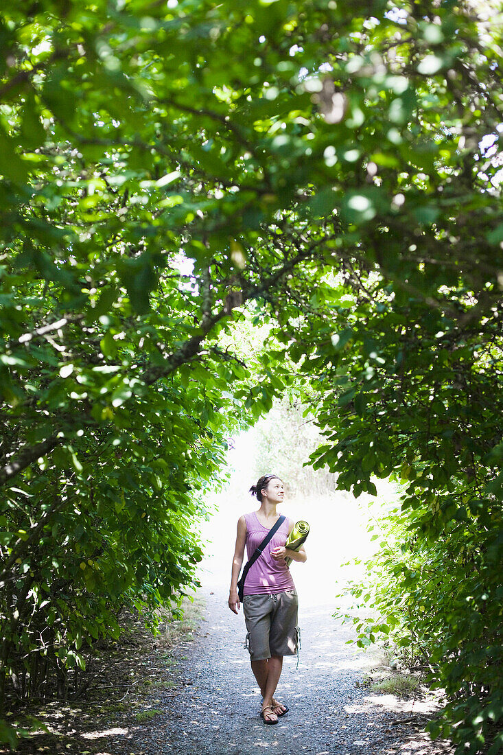 A young woman stands in an arch of greenery while holding her yoga mat Seattle, Washington, USA