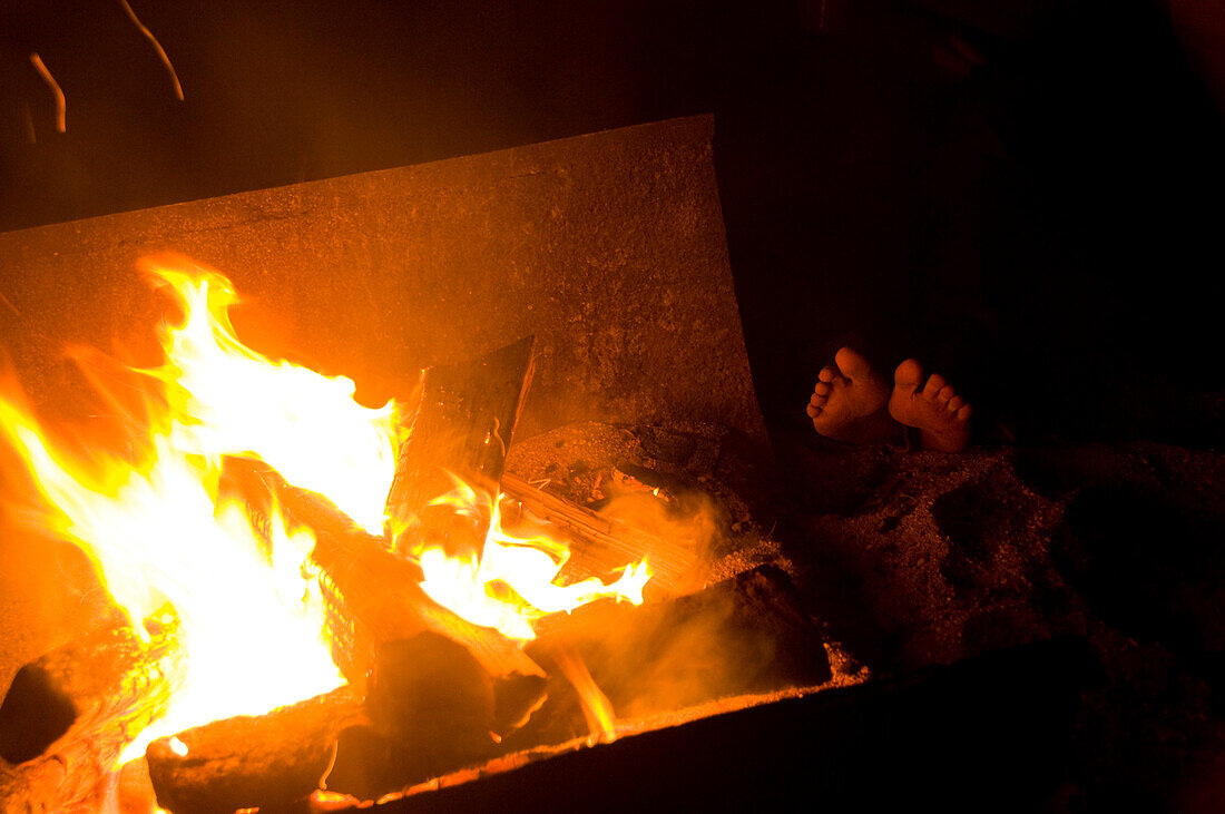 Feet warm by an open campfire, Lake Sebago, Maine Lake Sebago, Maine, USA